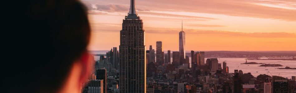 Person views new york city skyline at vibrant sunset.