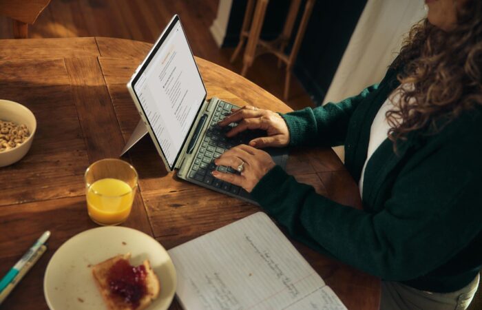 Woman typing on laptop at wooden table with breakfast.